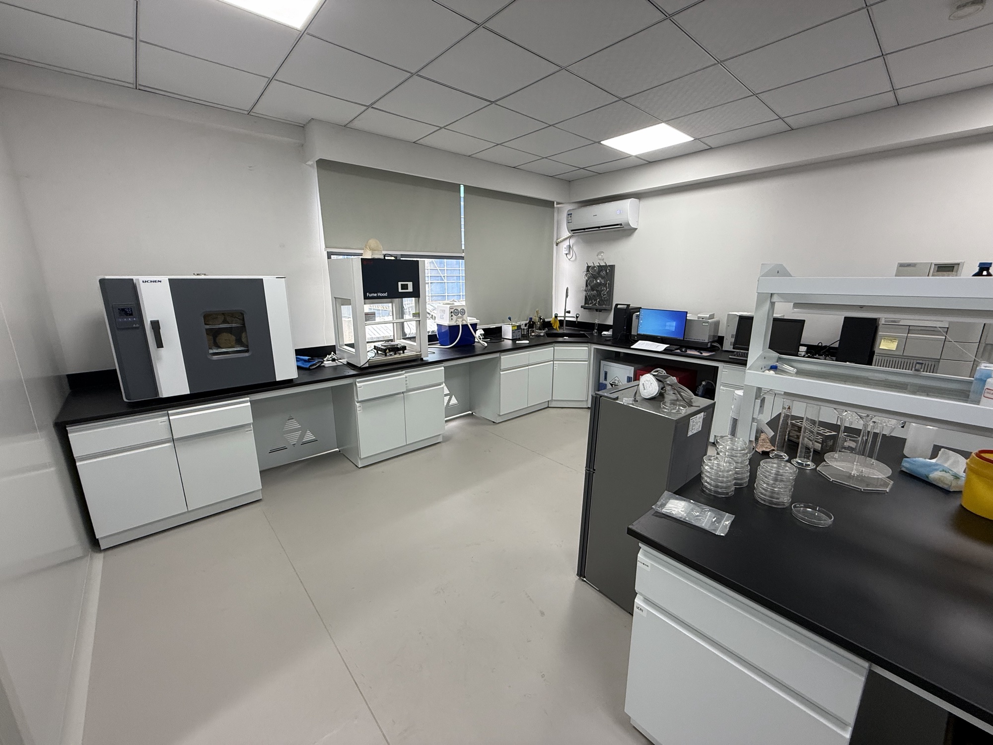 Laboratory equipment, glassware and white cabinets around an L-shaped workbench.
