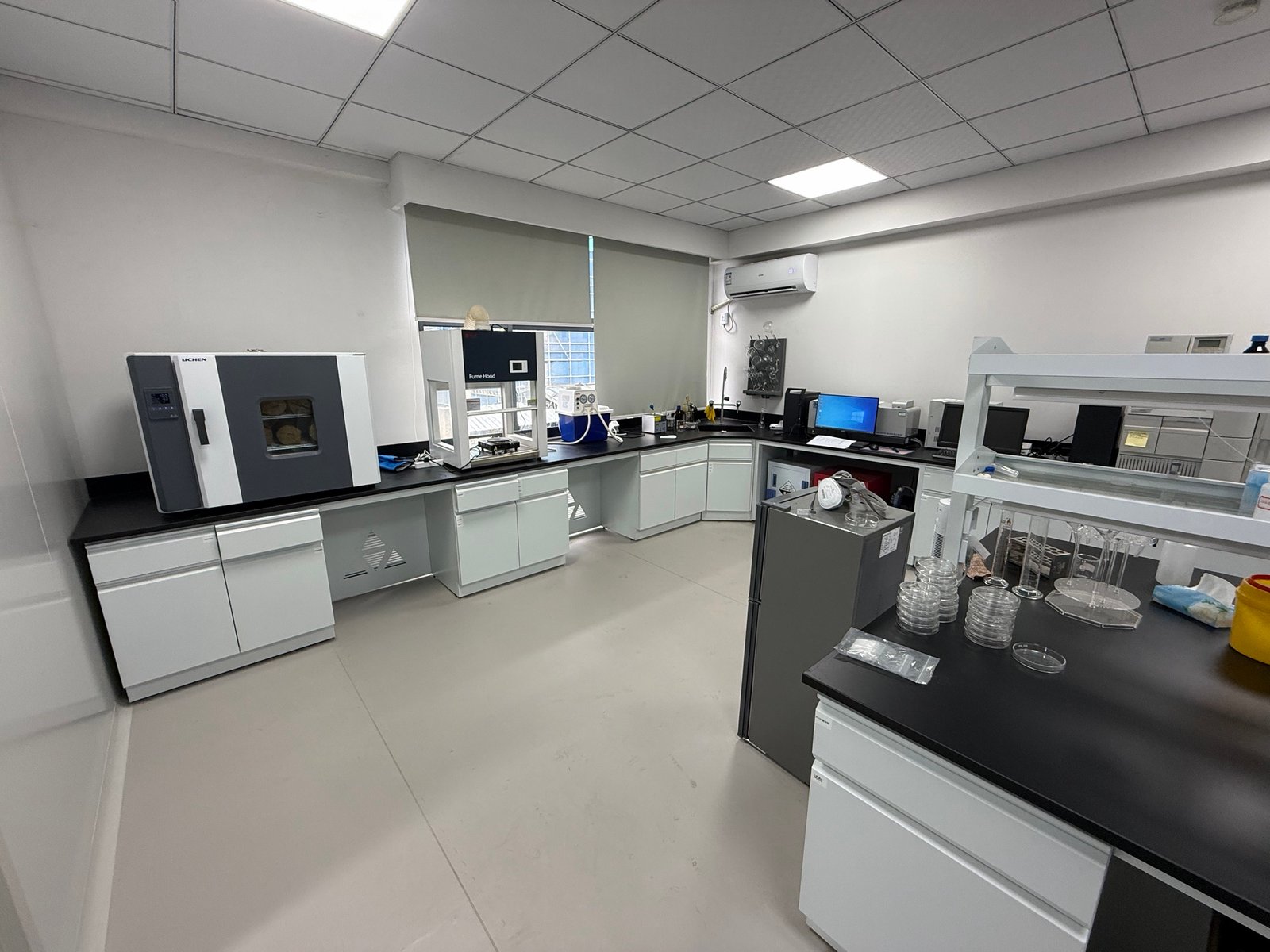 Laboratory equipment, glassware and white cabinets around an L-shaped workbench.